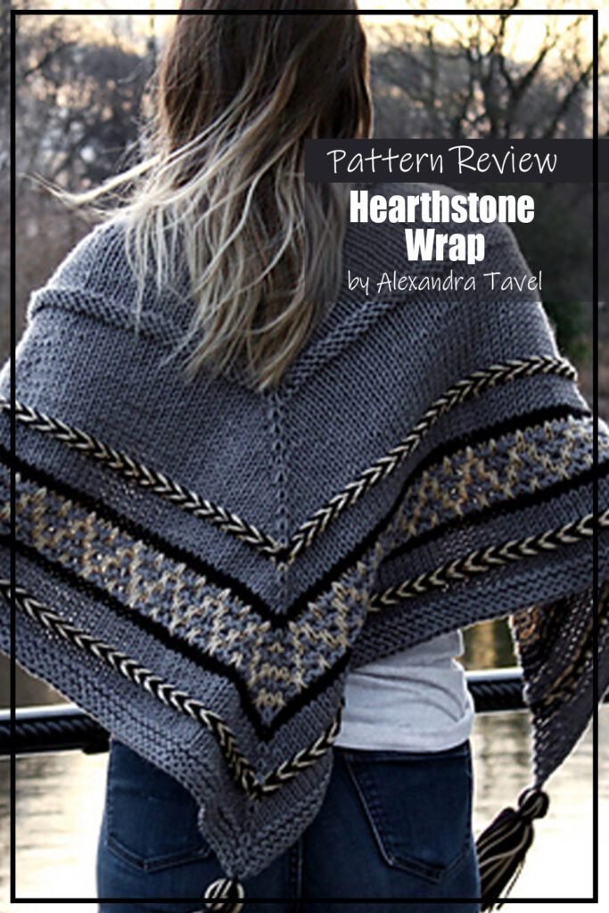 Hearthstone Wrap by Alexandra Tavel knitting pattern sample made with a dark grey yarn for the main body with accents of black and cream. Modeled on a woman wearing jeans and a white long sleeve shirt, the picture shows the wrap draped across her back. Text on the image says "Hearthstone Wrap by Alexandra Taval Pattern Review"