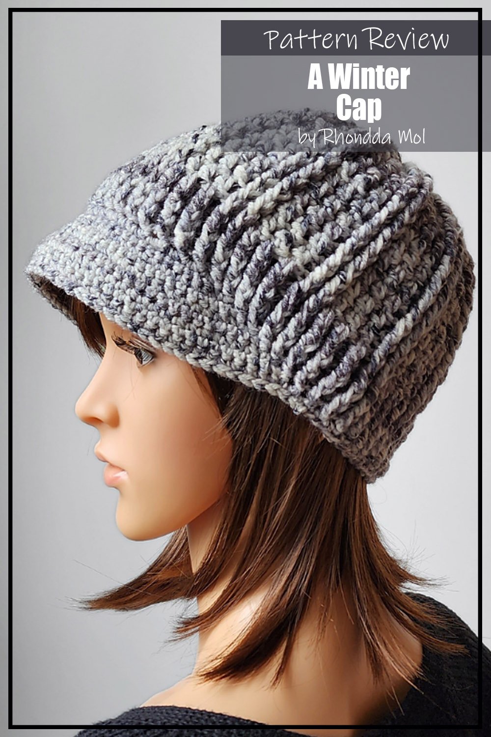 A Winter Cap crochet pattern sample is made using grey aran weight yarn. The hat features a cap style brim and a textured main body of the hat. It is modeled on a mannequin. The text on the image reads "A Winter Cap by Rhondda Mol Pattern Review".