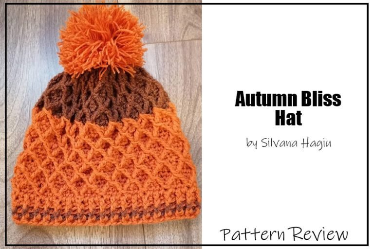 The Autumn Bliss hat crochet pattern sample is made using two colours of aran weight yarn. The cuff and most of the body of the hat is made with an orange yarn. The crown is made with a brown yarn. There is an orange pompom. The hat features a diamond stitch texture pattern maded using triple crochets. The text on the image reads "Autumn Bliss Hat by Silvana Hagiu Pattern Review".