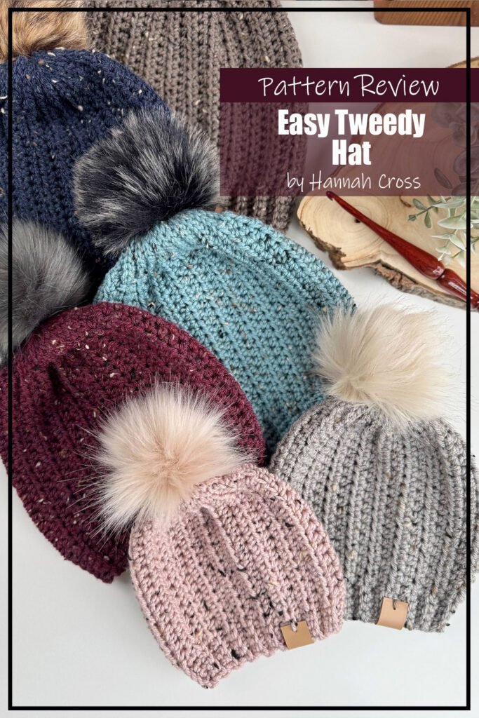 Easy Tweed Hat crochet pattern samples made in a variety of colours with furry pompoms on the tops. The hat samples are laying flat in a basket on a white surface. The text on the image reads "Easy Tweed Hat by Hannah Cross Pattern Review".
