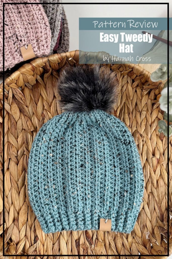 Easy Tweed Hat crochet pattern samples made in a aqua coloured yarn with furry pompom on the top. The hat sample is laying flat in a basket. The text on the image reads "Easy Tweed Hat by Hannah Cross Pattern Review".