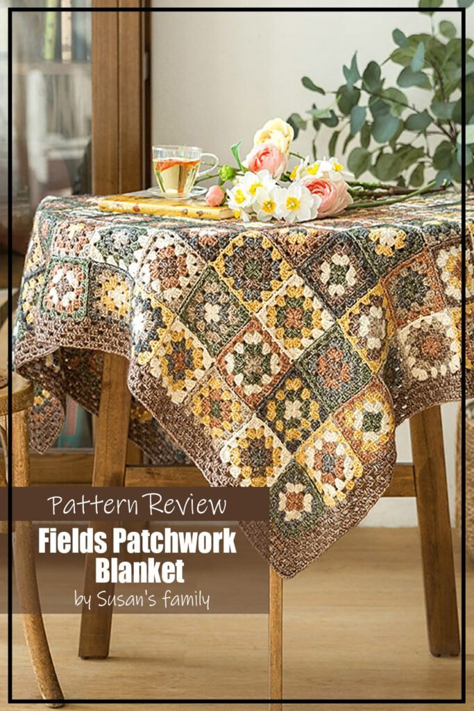Blanket crochet pattern sample is made using a beautiful collection of muted yet colourful yarns. Blue, green, brick red, and yellow is anchored with a brown. The blanket is draped over a table. The text on the image reads "Fields Patchwork Blanket by Susan's Family Pattern Review".