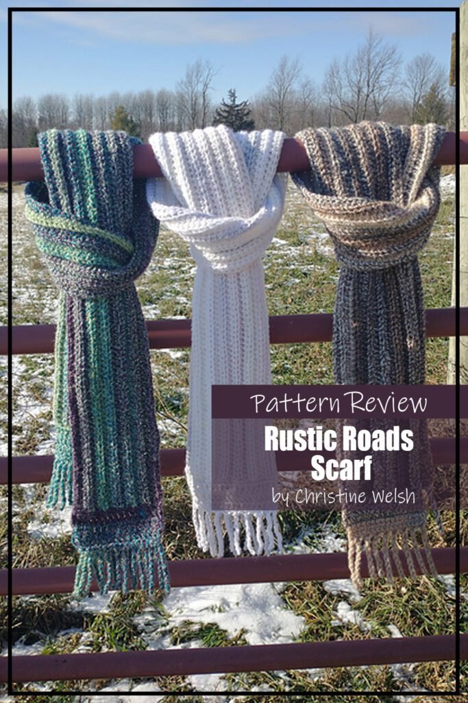 Rustic Roads Scarf crochet pattern samples are made with a white yarn, green and blue variegated yarn, and a brown variegated yarn. The crochet scarf samples are hanging on a fence. The text on the image reads "Rustic Roads Scarf by Christine Welsh Pattern Review."