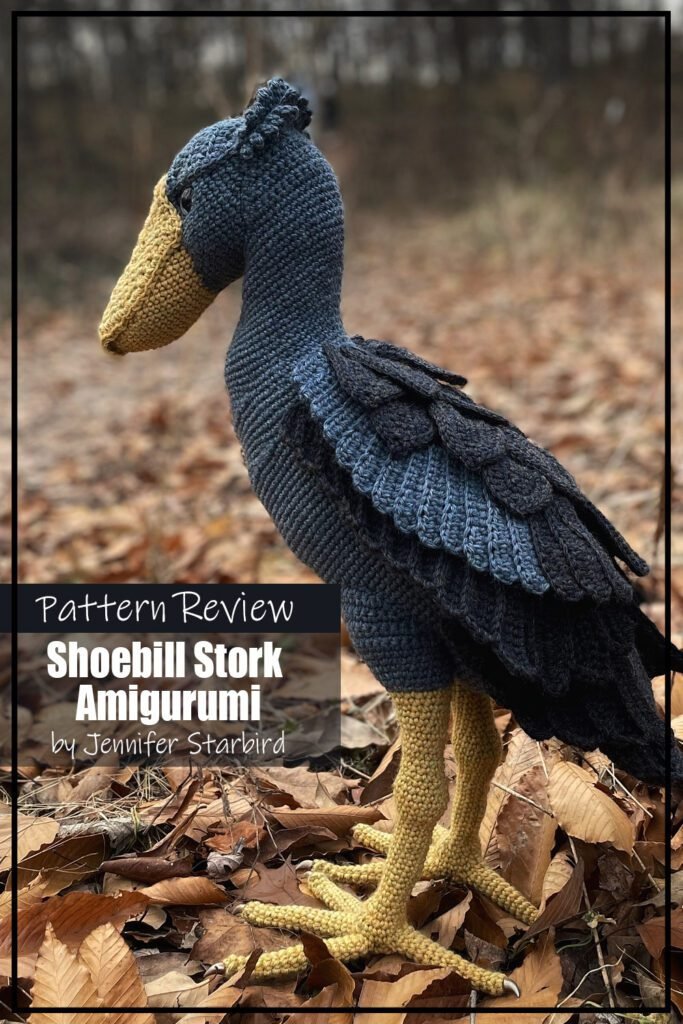 Shoebill Stork Amigurumi crochet pattern sample is maded with a grey/blue yarn with yellow beak and legs/feet. The crochet bird is photographed outside on leaf littered ground. The text reads "Shoebill Stork Amigurumi by Jennifer Starbird Pattern Review".