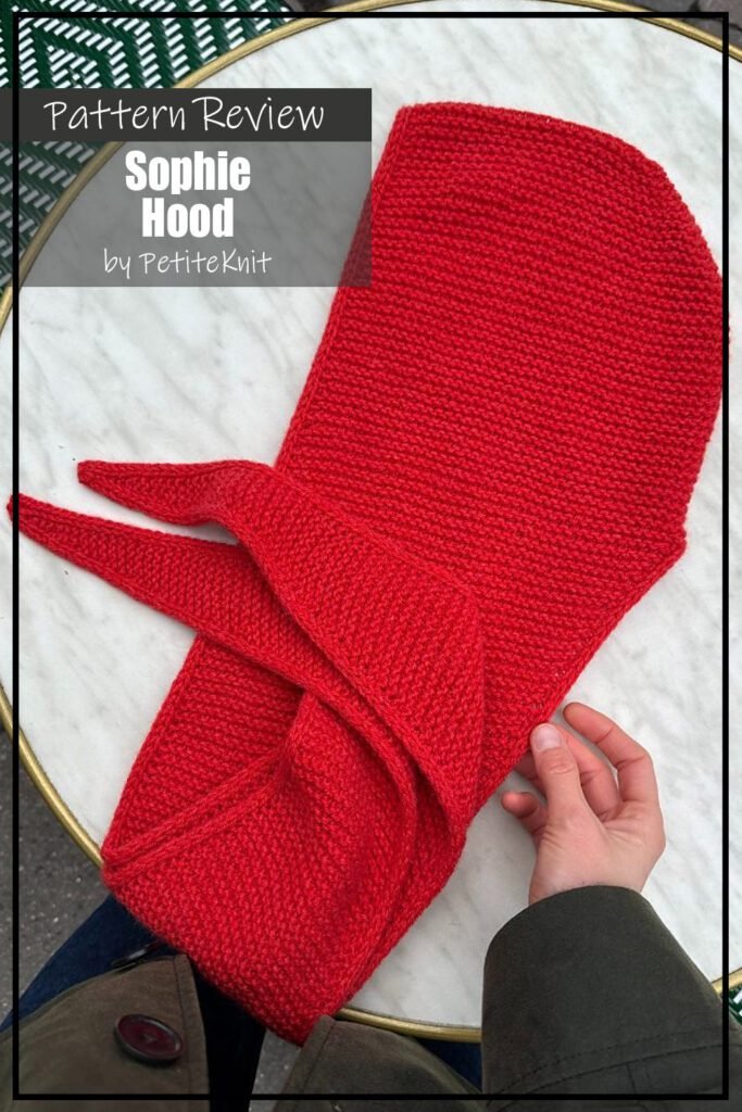 Sophie Hood knit pattern sample is made with red yarn and is laid flat on a white surface. Text on the image reads "Sophie Hood by PetiteKnits Pattern Review".